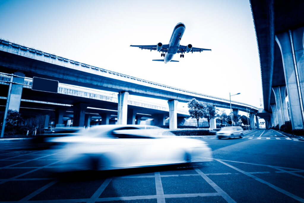 Airplane descending over highway overpasses with blurred cars below, capturing airport transportation and travel movement.